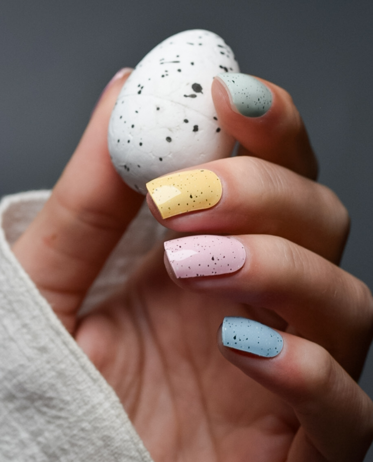 Hand mit Candy Eggshell UV Gel Wraps in Pastellfarben hält ein gesprenkeltes Ei