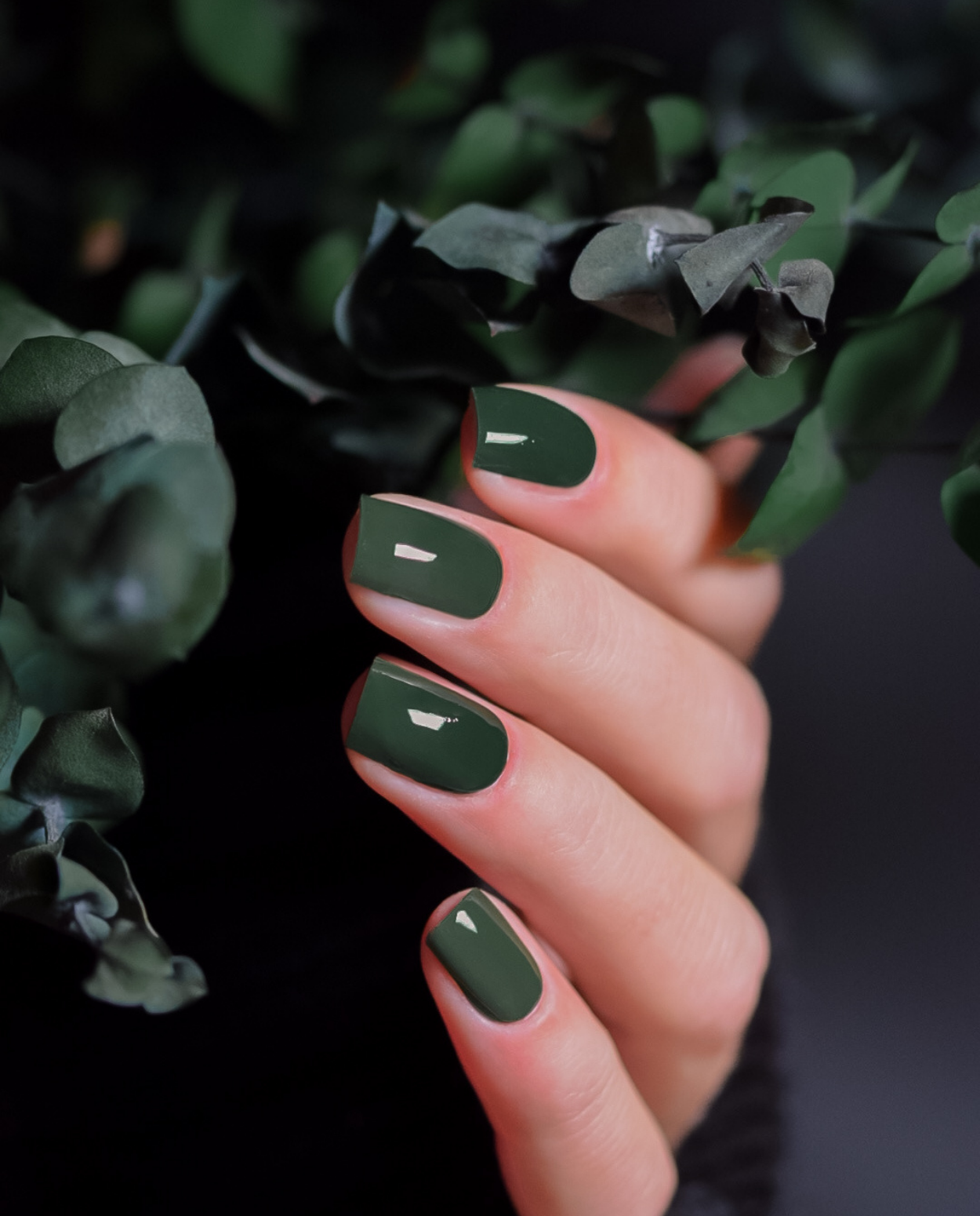 Maniküre mit Waldnebel – elegante Nägel in dunklem Grün, aufgenommen zwischen Blättern.