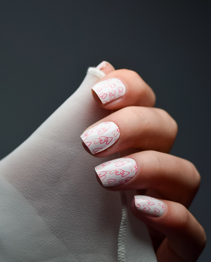 Hand mit UV Gel Wraps Herzstück – weiße Nägel mit pinken Herzchen-Motiven.