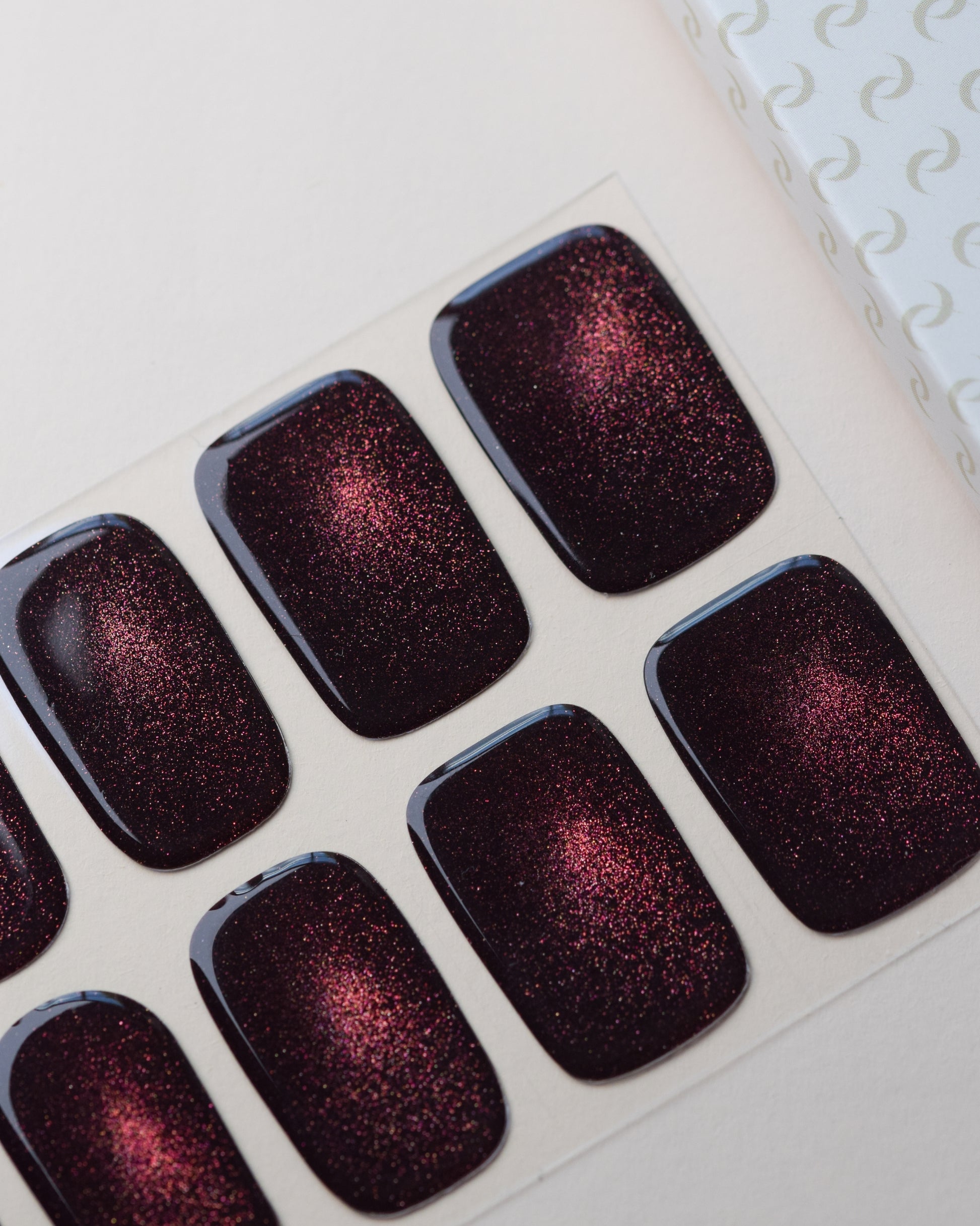 Burning Ruby Cat Eye UV Gel Wraps auf dem Designbogen mit rubinrotem Cat-Eye-Effekt und schimmernden Lichtreflexen.
