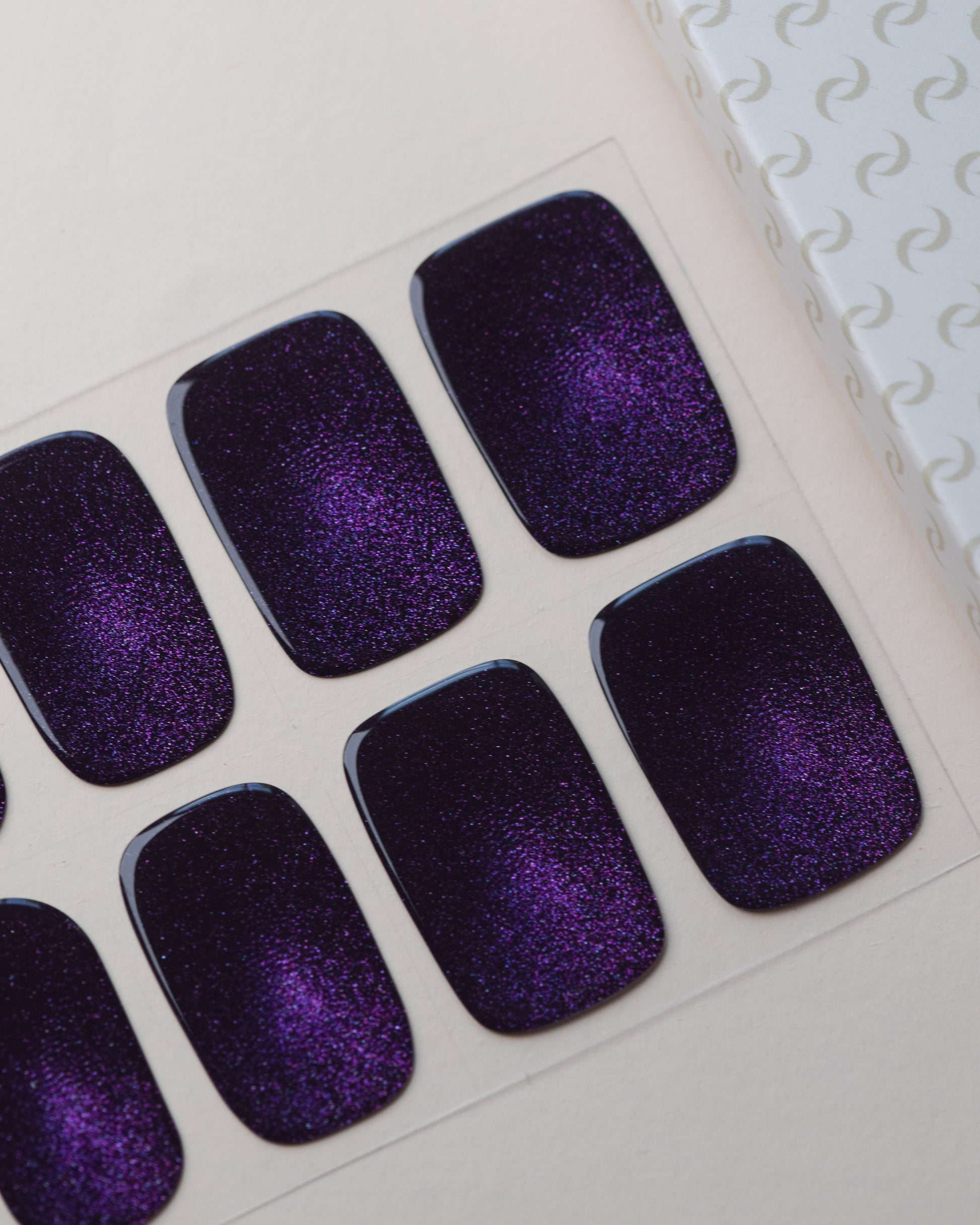 Cosmic Dust Cat Eye UV Gel Wraps auf dem Designbogen mit violettem Cat-Eye-Effekt und funkelndem Schimmer.