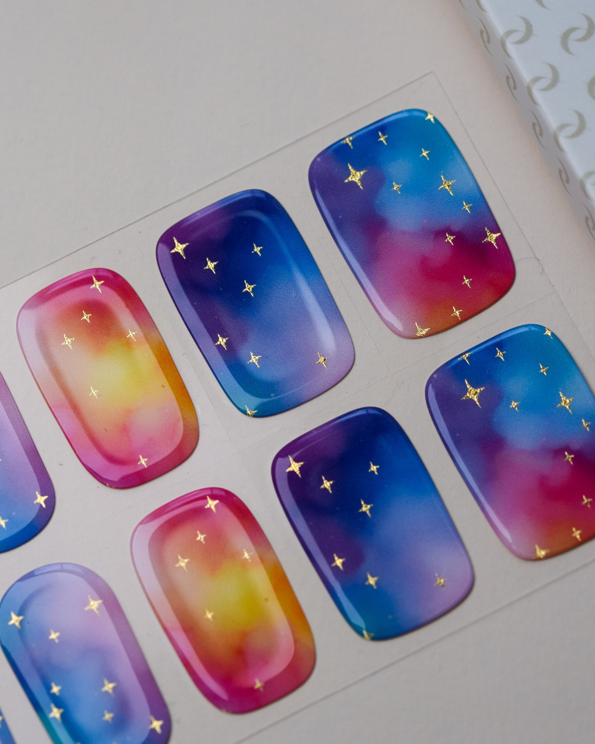 Detailaufnahme der Cotton Candy Cosmos Nailpolish Wraps mit Farbverläufen in Blau, Pink und Violett sowie goldenen Metallic-Sternen.