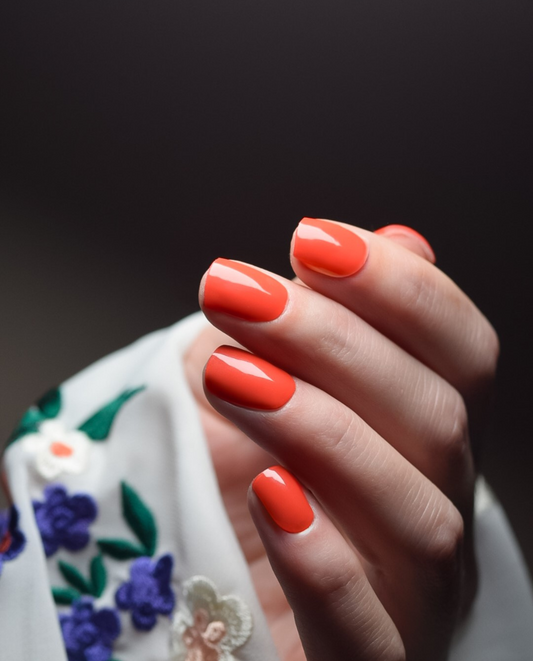 Heatwave UV Gel Wraps in leuchtendem Neonorange auf kurzen Nägeln, elegante Handpose mit floralem Stoff im Hintergrund.