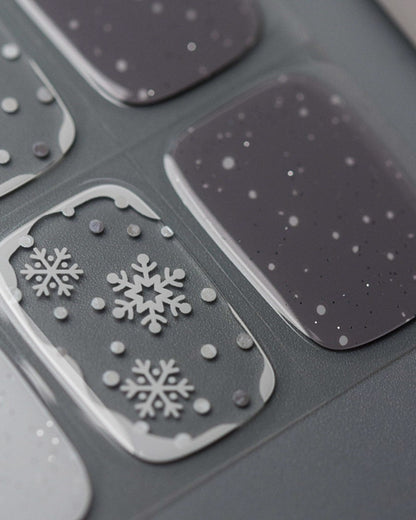 Nahaufnahme der Schneegrau UV Gel Wraps – kühle Grautöne, weiße Schneeflocken und dezente Golddetails für einen edlen Winterlook.
