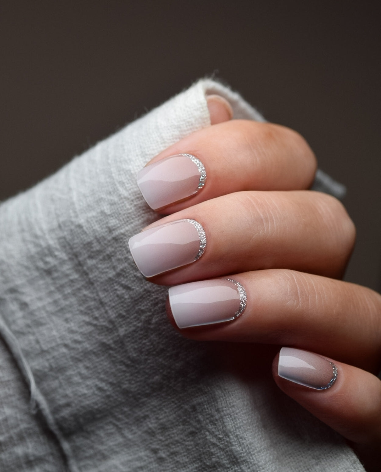 Hand mit UV Gel Wraps Babyboomer Nude Glitter – Nude-Ombré Nägel mit silbernem Glitzer-Rand.