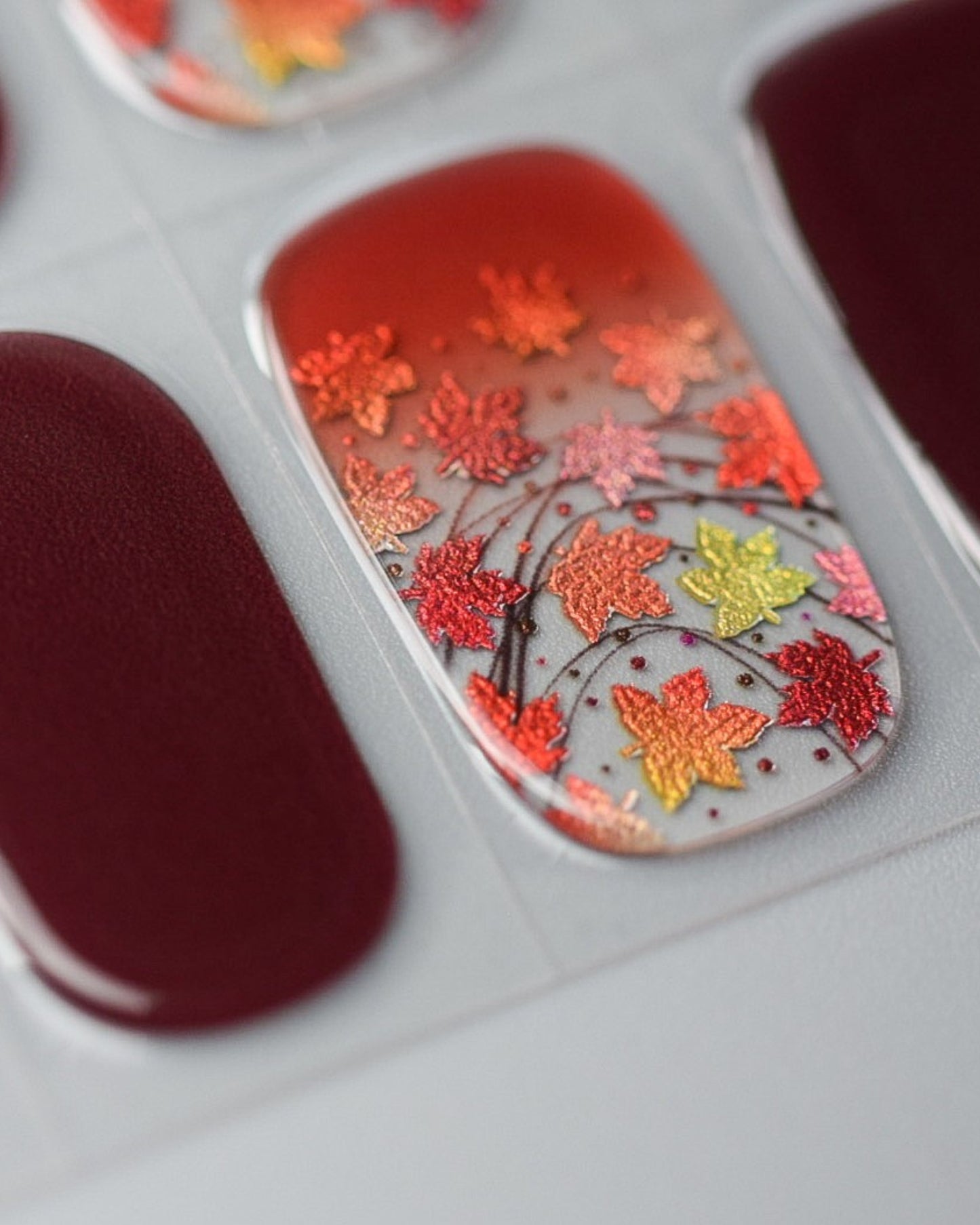Nahaufnahme der Ahornfeuer UV Gel Wraps – leuchtende Herbstfarben mit filigranen Blättermotiven und glitzernden Akzenten.

