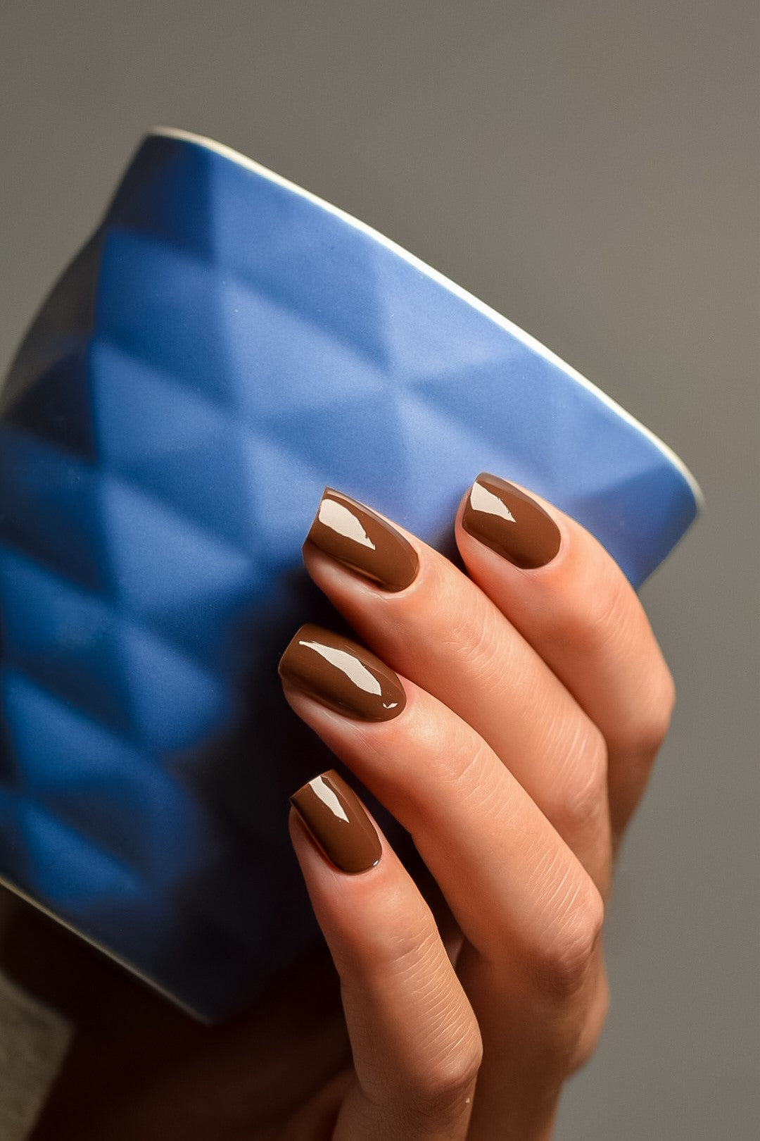 Hand mit UV Gel Wraps Mocha und blauem Becher in der Hand – dunkelbraune Nägel im Kaffeeton.