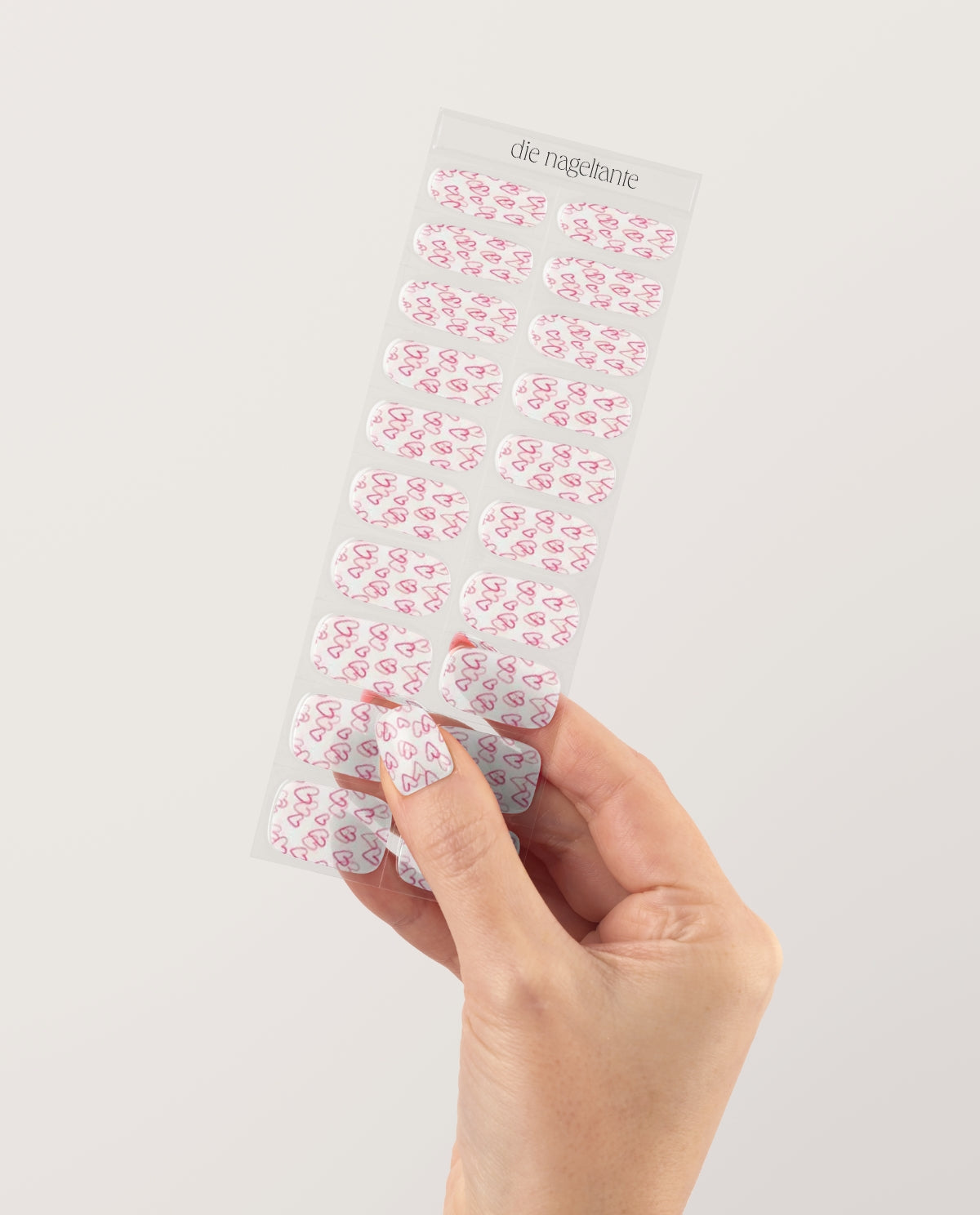 Hand mit UV Gel Wraps Herzstück – weiße Nägel mit pinken Herzchen-Motiven.