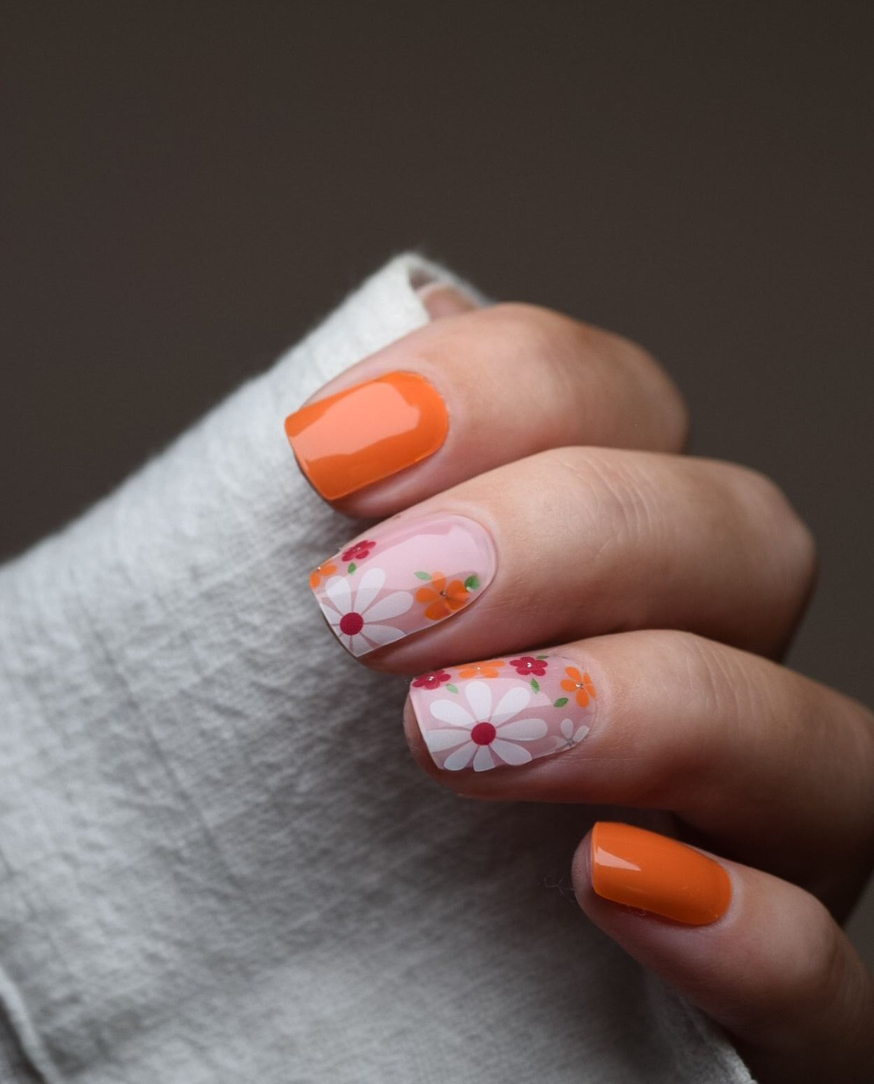 Hand mit UV Gel Wraps Orange Blossom – Orange Nägel mit floralen Akzentnägeln.