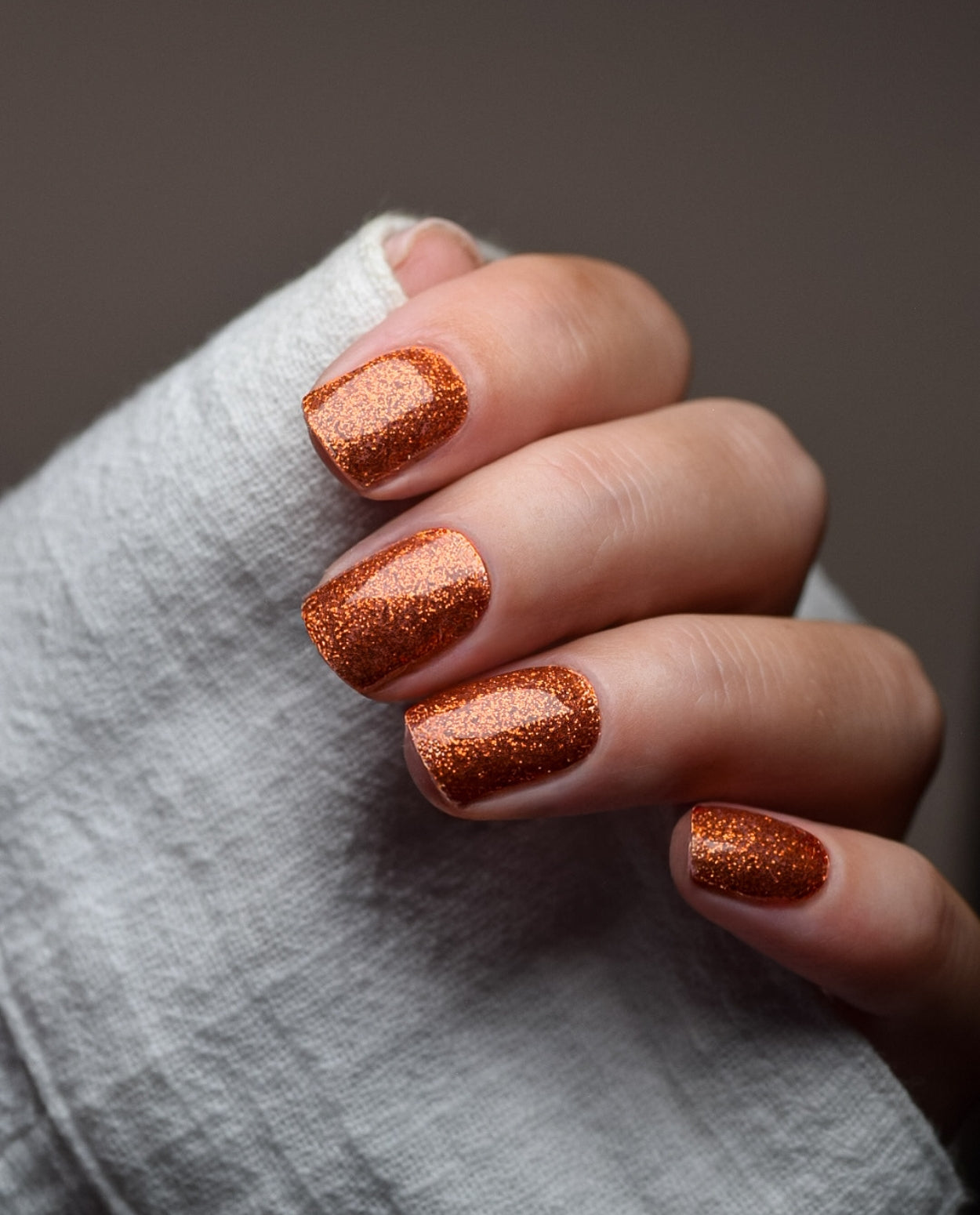 Hand mit UV Gel Wraps Copper Crush – kupferfarbene Glitzer-Nägel mit glänzendem Finish.
