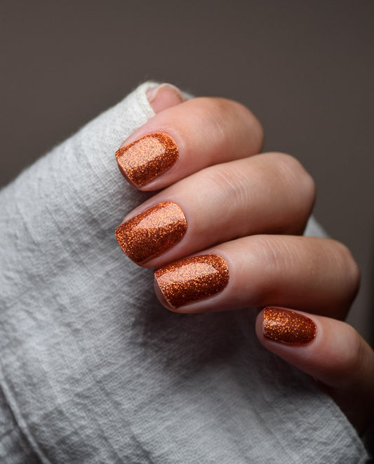 Hand mit UV Gel Wraps Copper Crush – kupferfarbene Glitzer-Nägel mit glänzendem Finish.