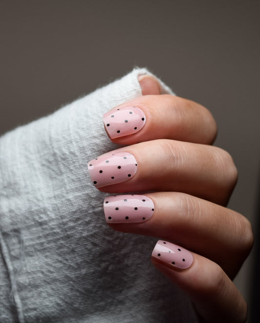 Hand mit UV Gel Wraps Dot Couture – Nude-Rosé Nägel mit schwarzen Punkten.