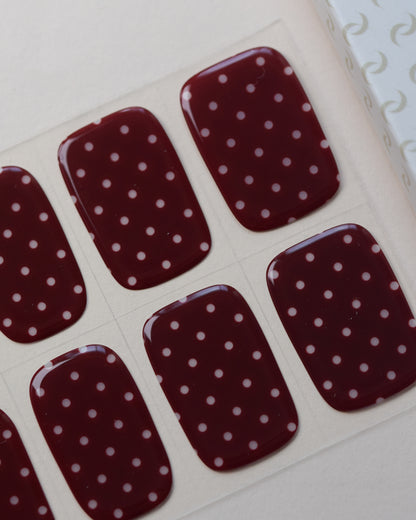 Ruby Dots UV Gel Wraps auf dem Designbogen mit weißen Punkten auf dunkelrotem Hintergrund.